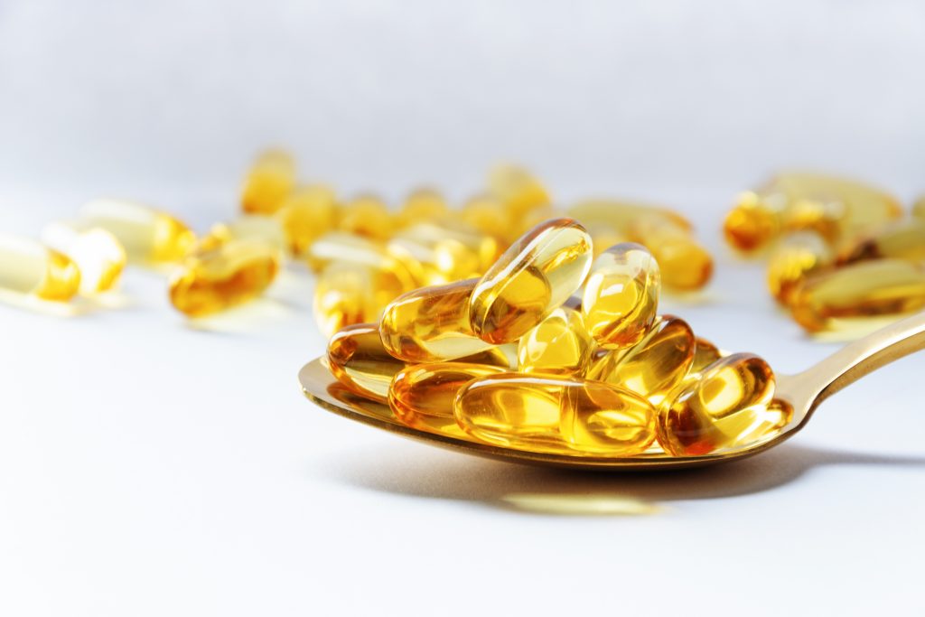 COD LIVER OIL OMEGA 3 GEL CAPSULES ON A SPOON ON WHITE BACKGROUND. FISH OIL VITAMINS.
